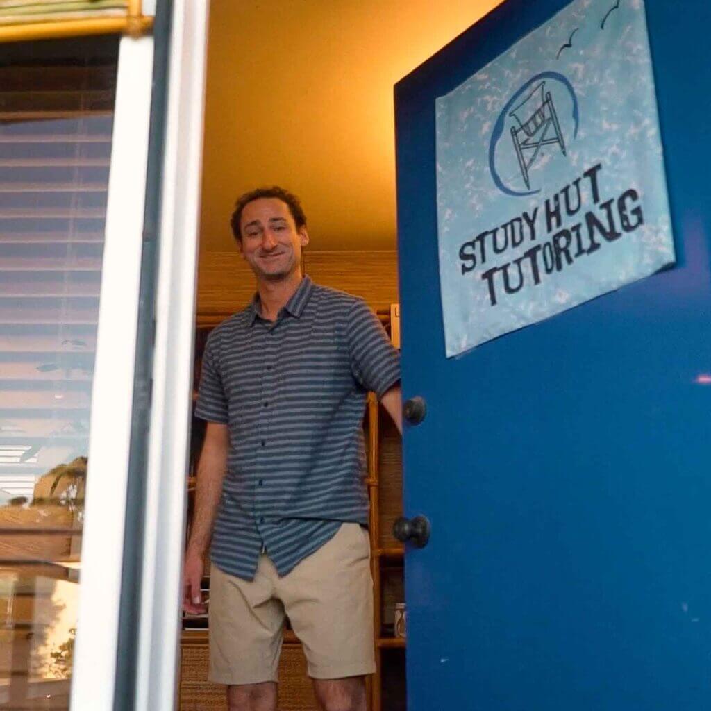 Friendly man welcoming students at the entrance of Study Hut Tutoring, a cozy academic support center with a beach-inspired vibe and personalized learning environment.